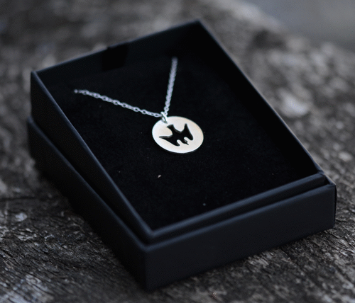 pendentif Colombe un pendentif en argent ajouré d'une colombe est dans un écrin sur du bois.