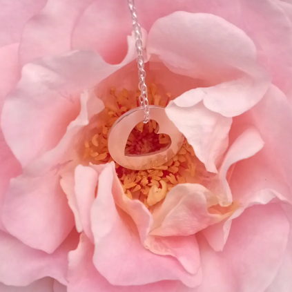 un pendentif en argent ajouré d'un coeur est posé devant une rose.