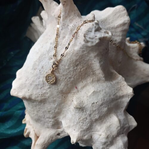 une chaine et un pendentif doré posés sur un coquillage