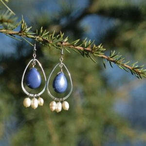 paire de boucles d'oreille avec une boucle, une pierre bleue et des perles sur une branche.