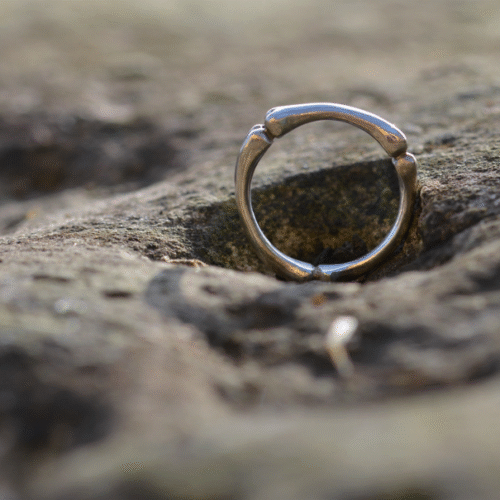 bague en argent formant trois os posée sur une pierre.