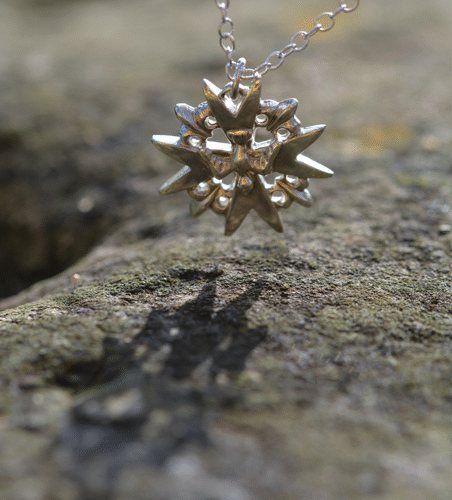 un pendentif croix de l'Esprit Saint en argent représentant une croix avec une colombe, pendant au dessus d'une pierre.