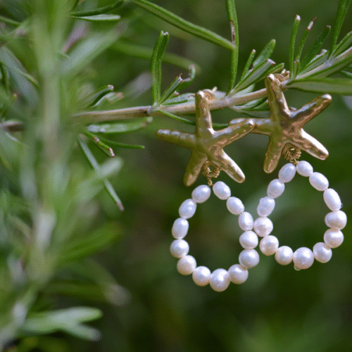 boucles d'oreille dorées en étoile de mer avec une boucle de perles de culture accrochées à une branche.