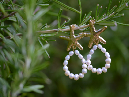 boucles d'oreille dorées en étoile de mer avec une boucle de perles de culture accrochées à une branche.