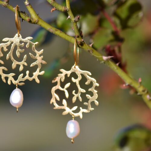 une paire de boucles d'oreilles dorées avec une perle accrochée sur une branche.