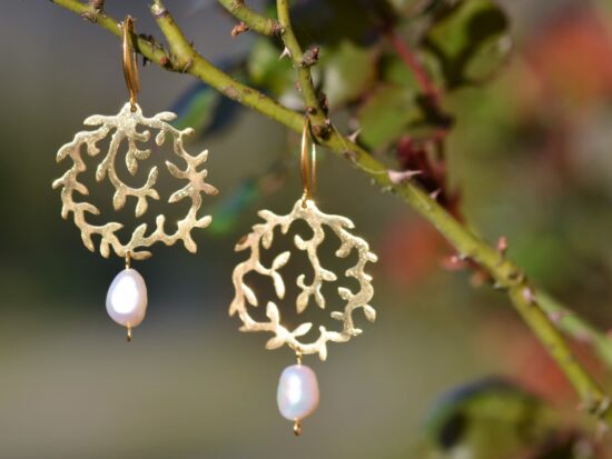 une paire de boucles d'oreilles dorées avec une perle accrochée sur une branche.