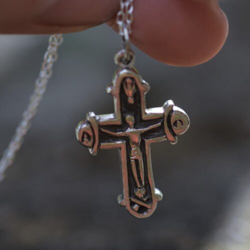 croix en argent sur une chaine tenue par une main.