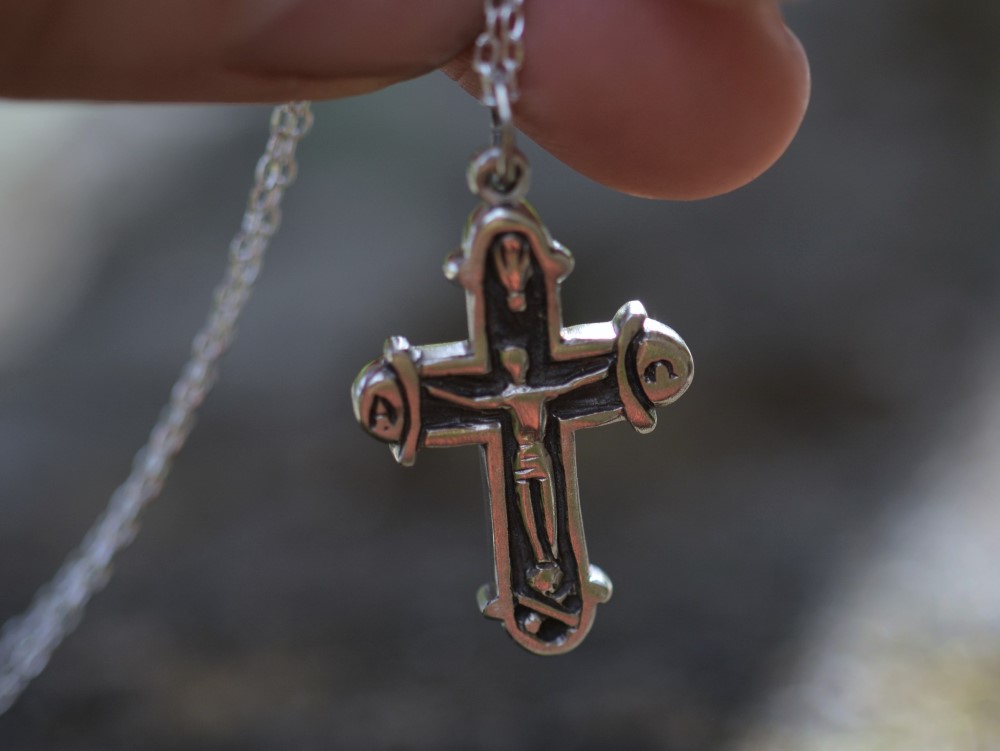 croix en argent sur une chaine tenue par une main.