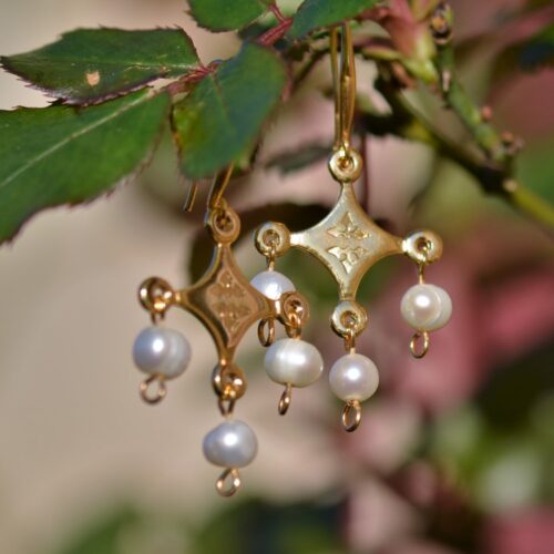 une paire de boucles d'oreilles dorées avec des perles accrochée sur une branche.