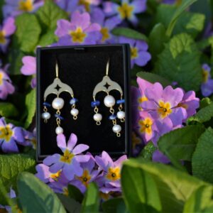 paire de boucles d'oreilles dorées avec des perles et des lapis, posée dans les fleurs.