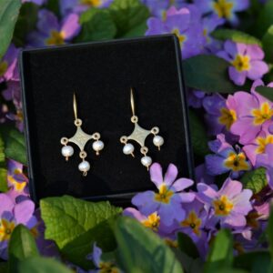 une paire de boucles d'oreilles dorées avec des perles posée dans les fleurs.