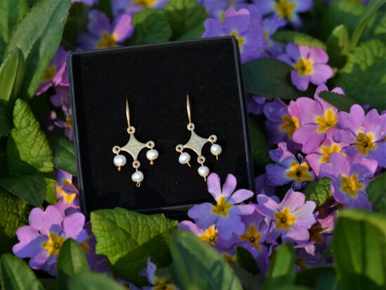 une paire de boucles d'oreilles dorées avec des perles posée dans les fleurs.
