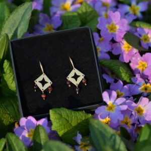 une paire de boucles d'oreilles dorées avec des perles en oeil de taureau posée dans les fleurs.