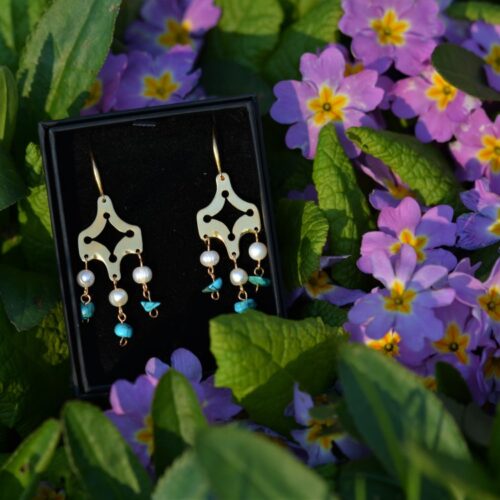paire de boucles d'oreilles dorées avec des perles et des turquoises, posée dans les fleurs.