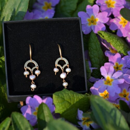 une paire de boucles d'oreilles dorées avec des perles de culture posée dans les fleurs.