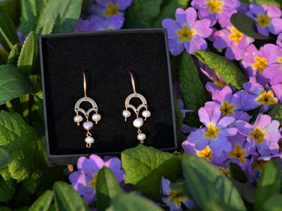 une paire de boucles d'oreilles dorées avec des perles de culture posée dans les fleurs.