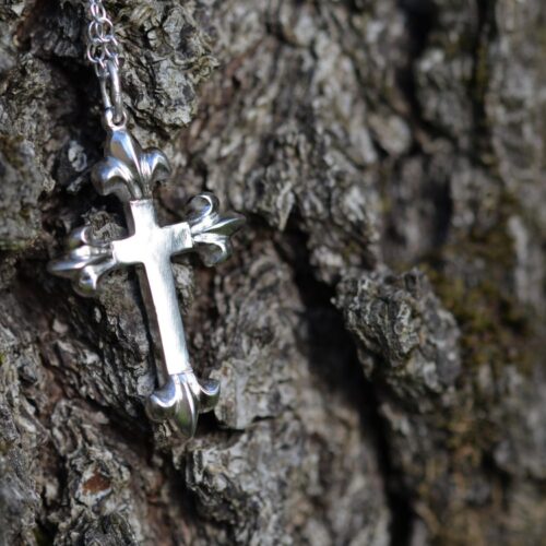 croix en argent avec 4 fleurs de lys sur chaque extrémité, posé sur de l'écorce.