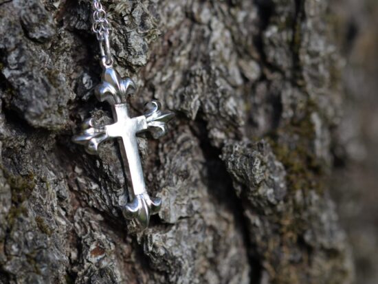 croix en argent avec 4 fleurs de lys sur chaque extrémité, posé sur de l'écorce.