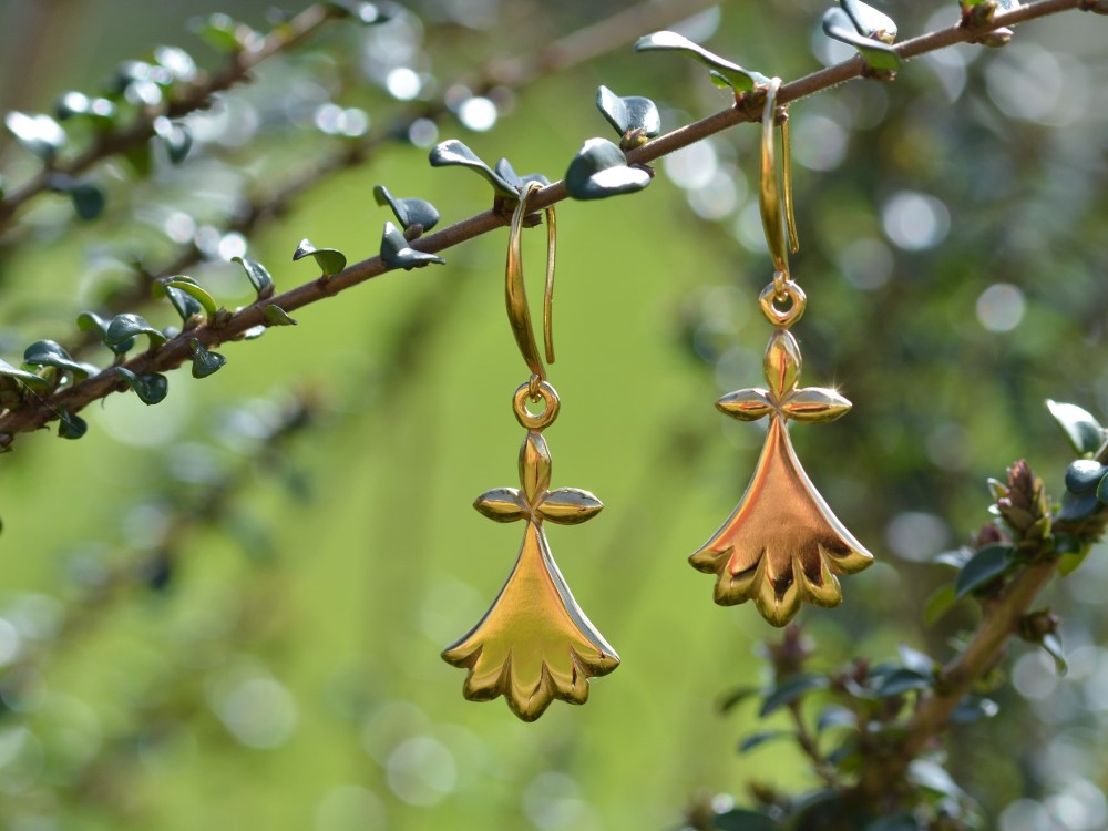 une paire de boucles d'oreilles dorées représentant des hermines accrochée sur une branche.