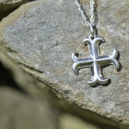pendentif croix ancrée en argent posé sur une pierre.