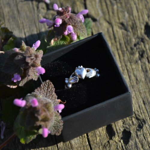 bague avec deux main tenant un coeur couronné dans un écrin.