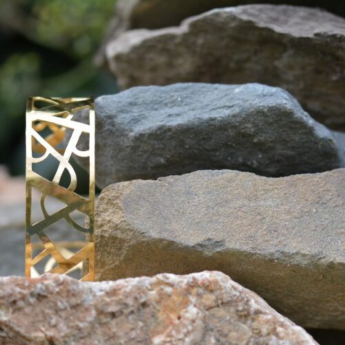 bracelet doré ajouré style art déco posé sur une pierre, Manchette Arcs et lignes