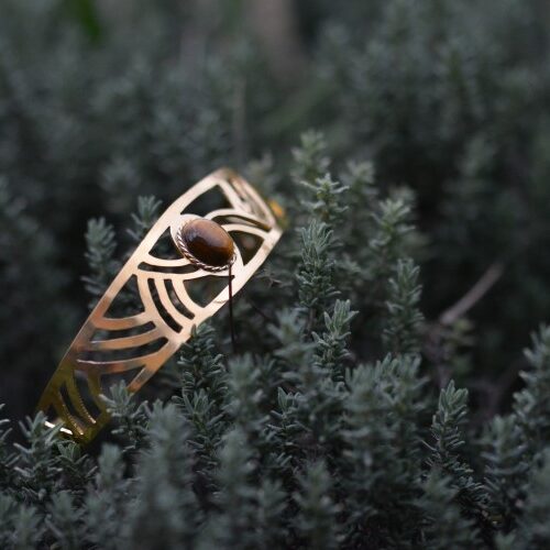 manchette Arceaux dorée ajourée style art déco posé dans une plante avec un oeil de tigre.