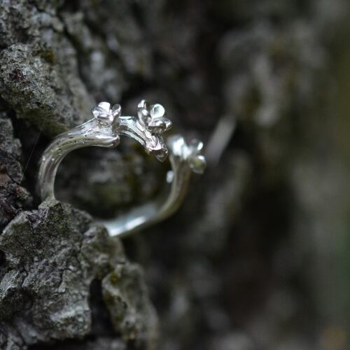 bague trois fleurs en argent posée sur un tronc d'arbre